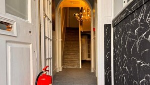A hallway with a fire extinguisher, a chandelier, and a staircase leading to another room. - Sachi Hotel (Brighton)
