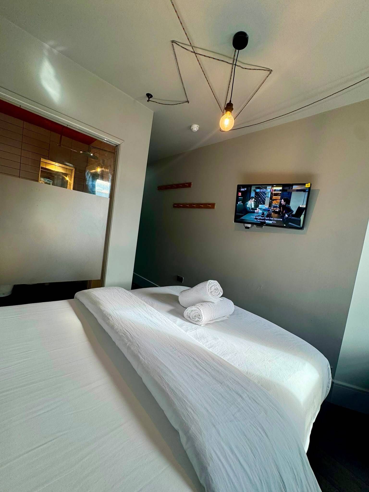 Ein Hotelzimmer mit einem Bett, einem an der Wand montierten Fernseher und einer Deckenleuchte.