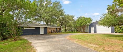 A residential driveway leading to a house with a garage, surrounded by trees and a grassy lawn.
