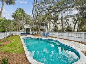 Piscina com borda curva, cercada por uma cerca branca, e área de deck com cadeiras azuis.