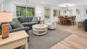 Een ruime woonkamer met een grijze bank, een ronde salontafel en een eettafel met stoelen.