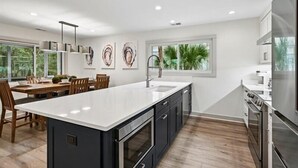 Een moderne keuken met een groot kookeiland, donkere kastjes en uitzicht op groen buiten het raam.