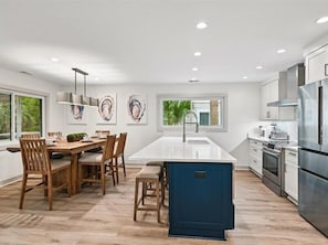 Cozinha moderna com ilha central, mesa de jantar de madeira e cadeiras.