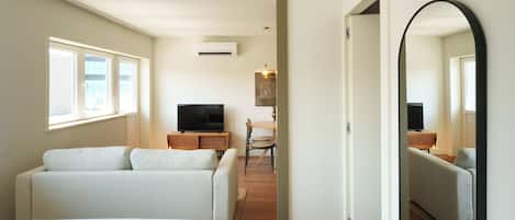 Ein Hotelzimmer mit Bett, einer Sitzecke, einem Fernseher, einem Essbereich mit Tisch und Stühlen sowie einem großen Spiegel.
