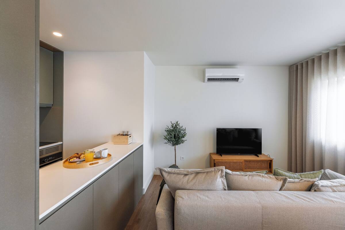 Una habitación de hotel moderna con una cama, un televisor, una mesita de madera, una planta y una bandeja para el desayuno en el mostrador.