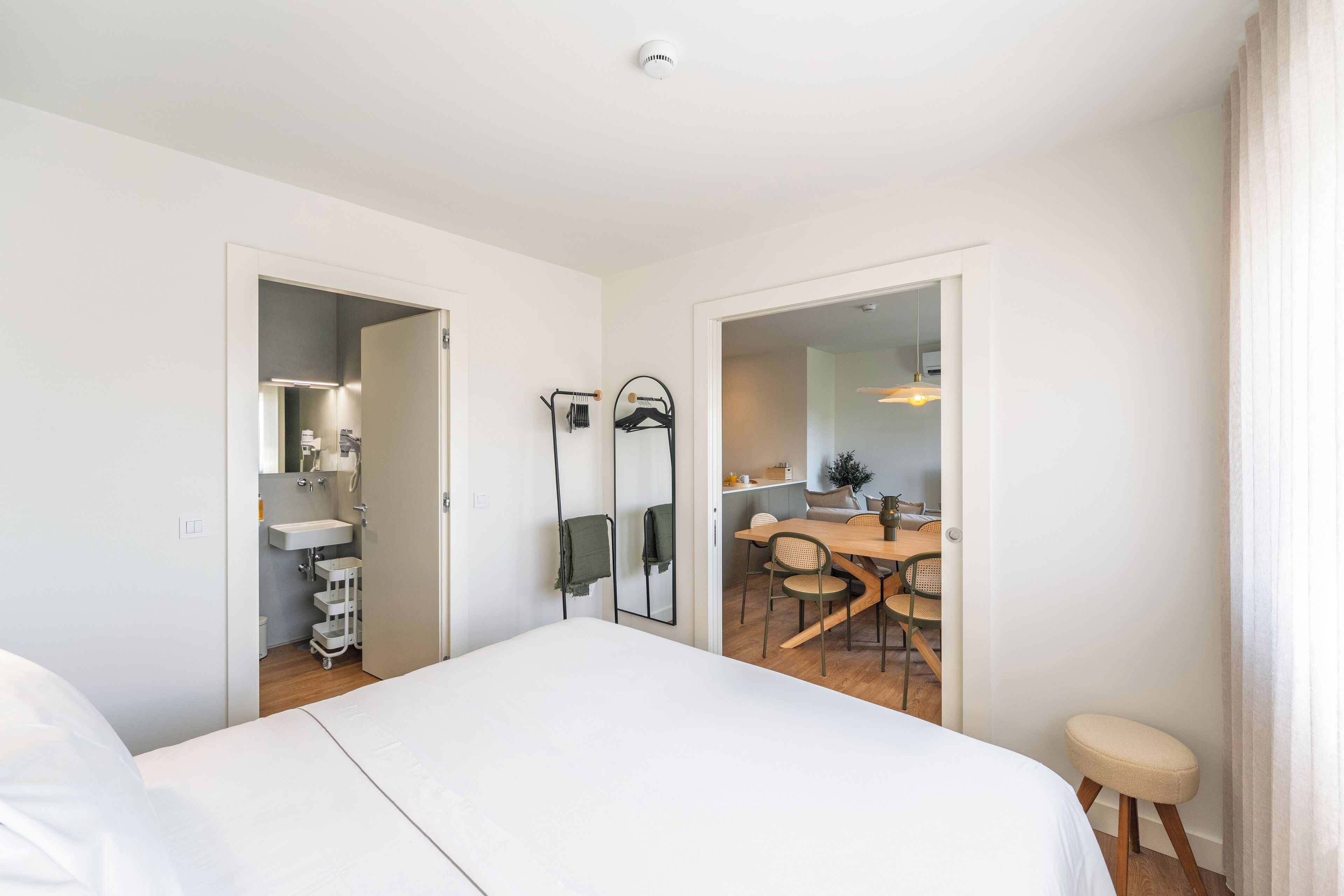 Ett modernt hotellrum med en stor säng, ett badrum med handfat och spegel samt en matplats med bord och stolar.