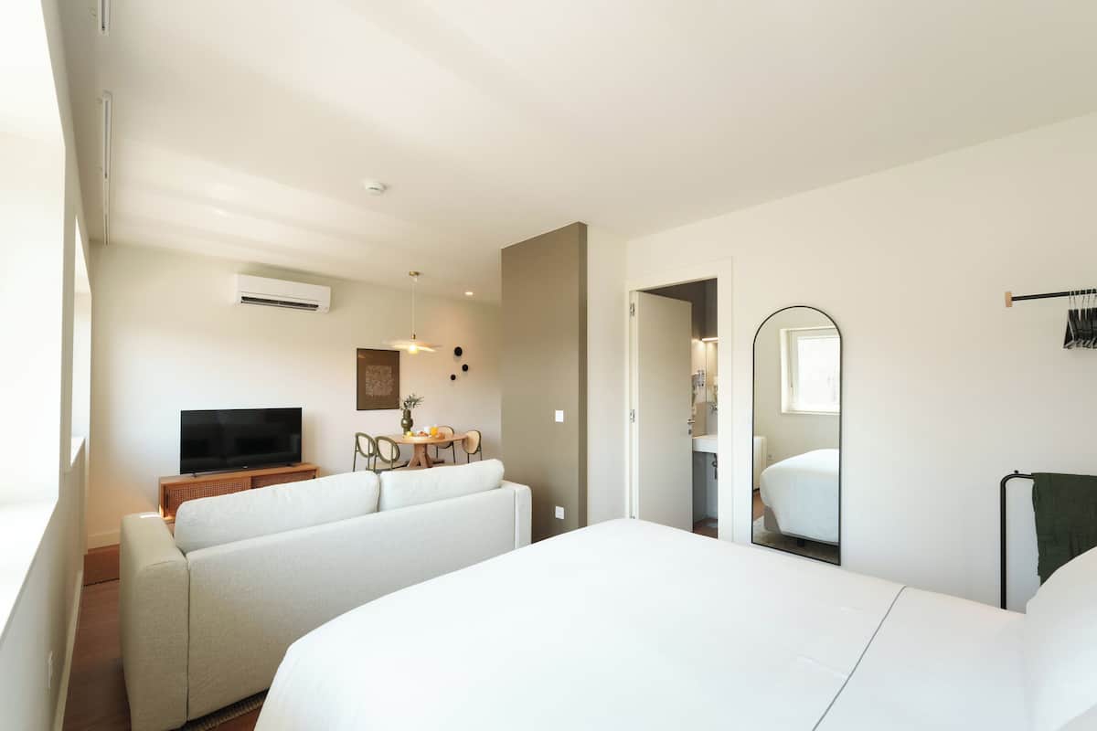 Una habitación de hotel moderna con una cama grande, un área de descanso con televisor y una mesa de comedor.