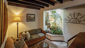 Een gezellige woonkamer met een bank, een lamp en uitzicht op een tuin door een raam.