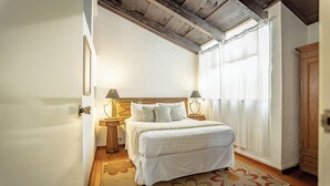 Een slaapkamer met een bed, twee nachtkastjes, een venster met gordijnen en een houten plafond.
