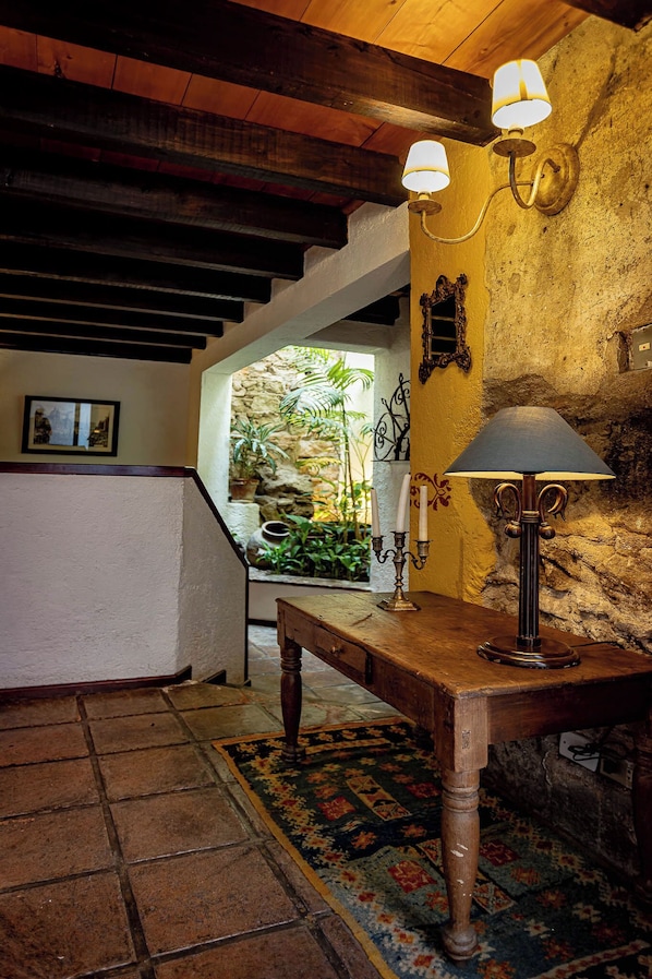 A rustic interior with a wooden table, a lamp, and a stone wall.