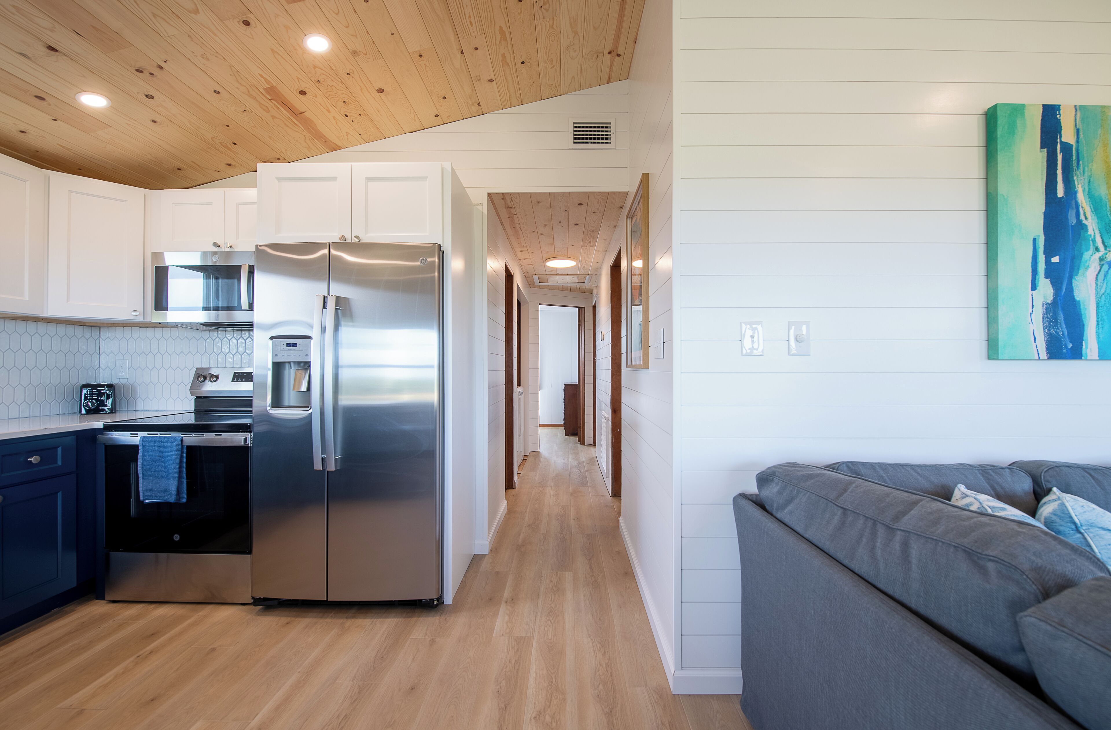 A modern kitchen with a stainless steel refrigerator, oven, and microwave. There is a gray sofa in the adjacent living area.