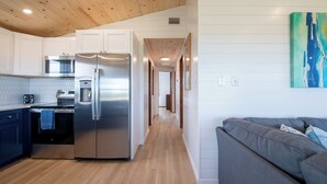 Una cocina moderna con refrigerador, horno y microondas de acero inoxidable. En el área de estar contigua, hay un sofá gris.