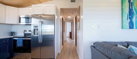 A modern kitchen with a stainless steel refrigerator, oven, and microwave. There is a gray sofa in the adjacent living area.