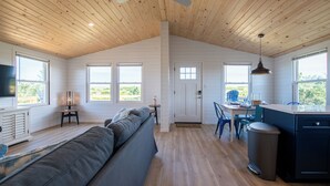 Amplia sala de estar con techo alto, vigas de madera, sofá, mesa de comedor y zona de cocina.