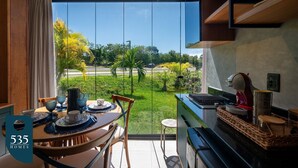 Uma cozinha moderna com uma janela grande, uma área de jantar com mesa posta para dois e vista para um jardim verde.