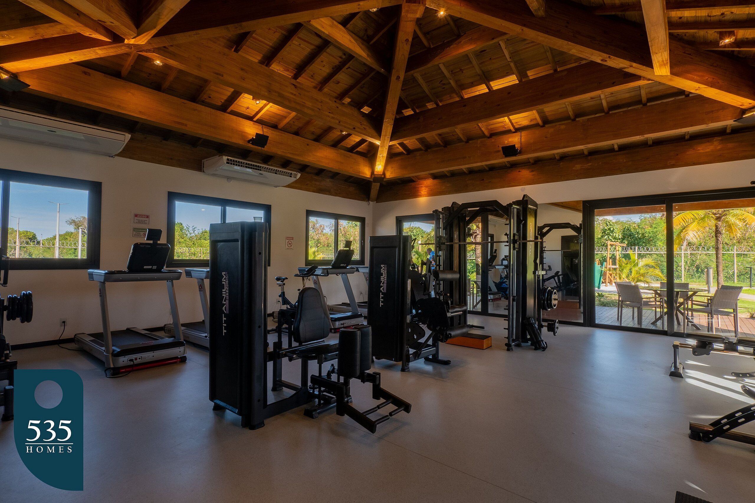 Une salle de sport spacieuse, dotée de divers appareils d’exercice, de grandes fenêtres et d’un plafond en bois.