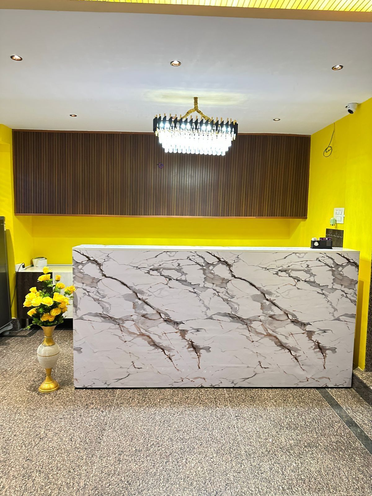 A reception desk with a marble top, a chandelier above, and a vase of yellow flowers to the left.