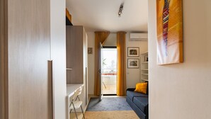 A compact living space with a kitchenette, a sofa with a yellow pillow, a dining area, and a view through a glass door. - GuestHost - La Casa di Polly (Bitritto)