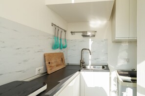 Una cucina moderna con una parete a schienale in marmo, un tagliere di legno, un lavandino e utensili da cucina color petrolio.