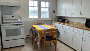 Une cuisine équipée d’un four à deux cavités, d’une table à manger avec une nappe et de meubles de rangement blancs.