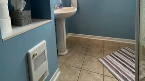 Une salle de bain avec un lavabo sur colonne, une fenêtre, un radiateur et des étagères contenant des articles de toilette.