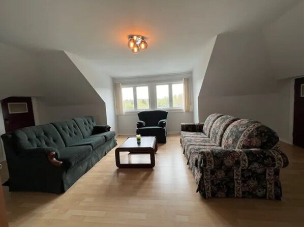Un loft spacieux avec un plafond haut, deux canapés, une table basse et une grande fenêtre laissant entrer la lumière naturelle.