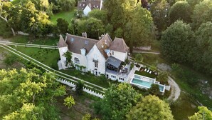 Uma grande mansão histórica com piscina, rodeada por vegetação exuberante e um jardim bem cuidado.