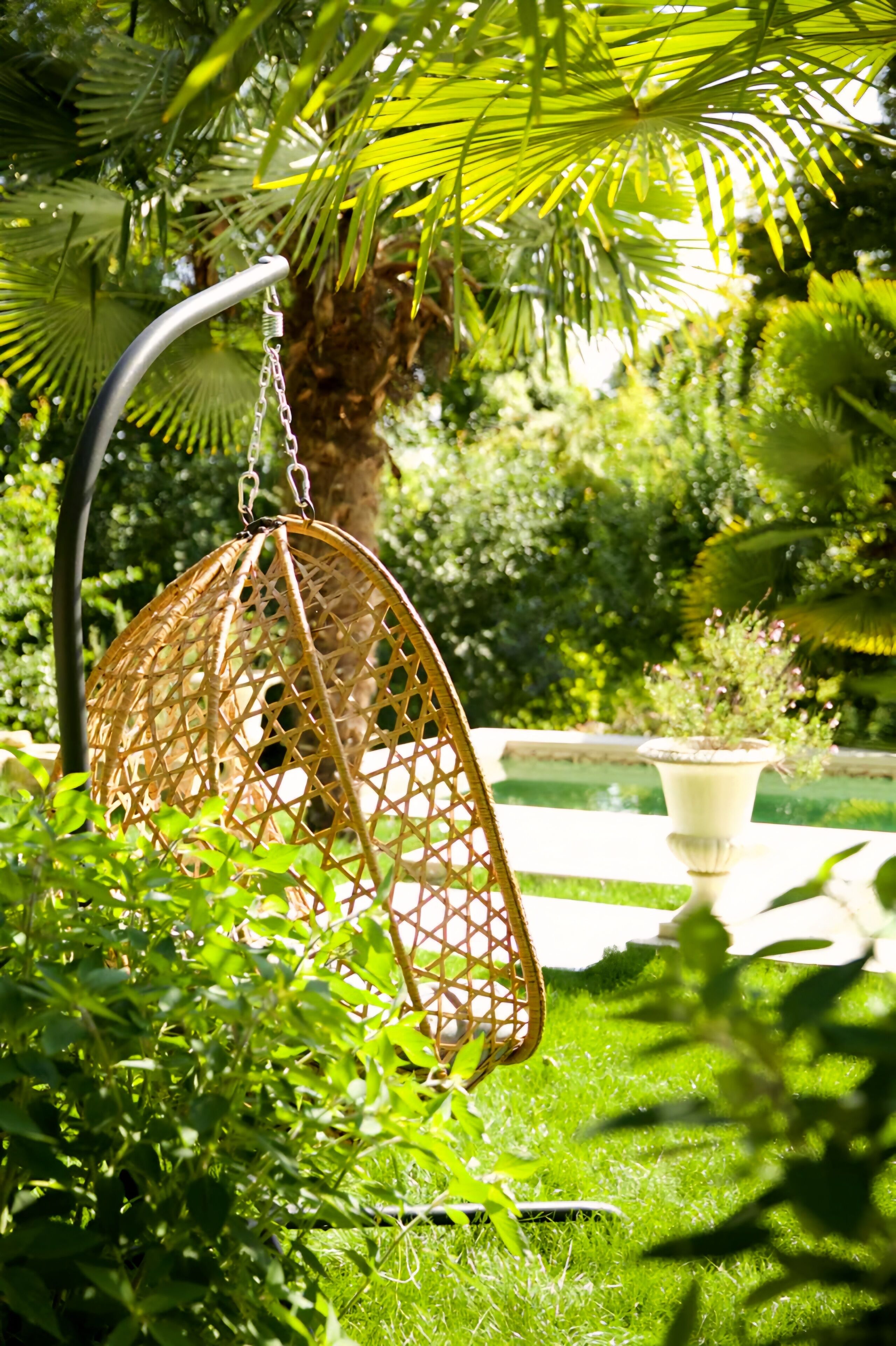 A hanging chair in a lush garden with a potted plant in the background.