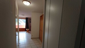 Ein schmaler Korridor mit Fliesenboden, einer Deckenleuchte und einer Tür zu einem anderen Raum.