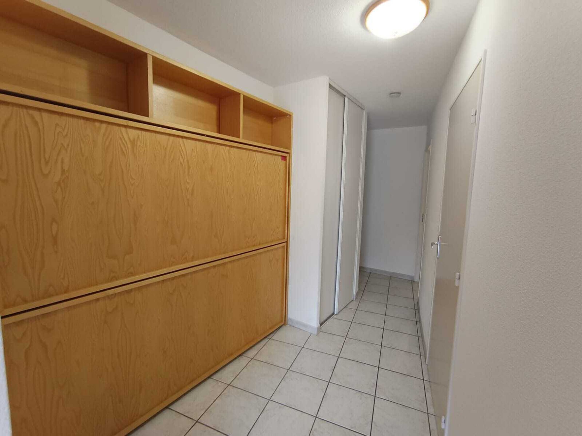 A hallway with wooden cabinets and a tiled floor.