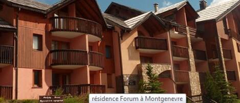 A multi-story residential building with balconies, stone accents, and a sign indicating it is a residence named Forum à Montgenèvre.