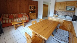 Ein gemütliches Wohnzimmer mit einem Holzsofa, einem Esstisch und einer Küchenzeile mit Holzschränken und einer Mikrowelle.