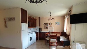 A living room with a sofa, a dining table, and a kitchen area with a washing machine. - Functional apartment for 5 people with pets allowed, parking and south-facing balcony (Montgenèvre)