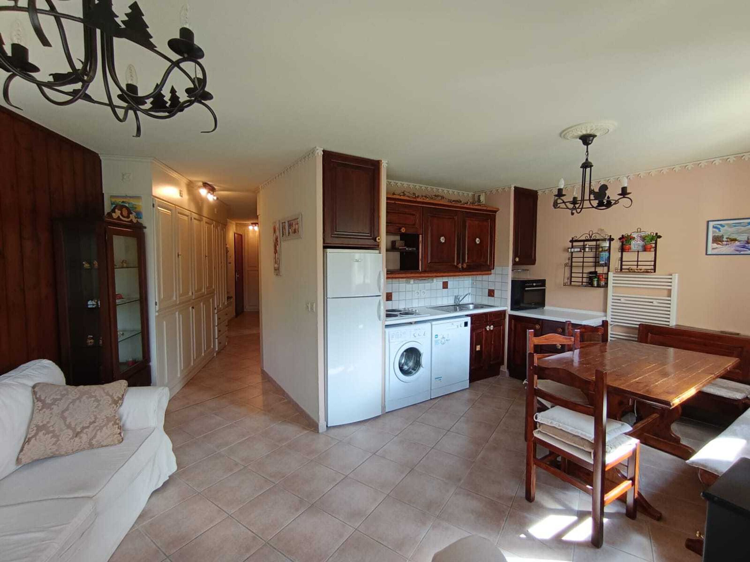 Uma cozinha compacta com máquina de lavar, sala de jantar com mesa e cadeiras de madeira e sala de estar com sofá.