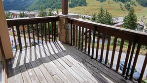 A wooden deck with a stone pillar, overlooking a mountainous landscape with a town below. - Functional apartment for 5 people with pets allowed, parking and south-facing balcony (Montgenèvre)