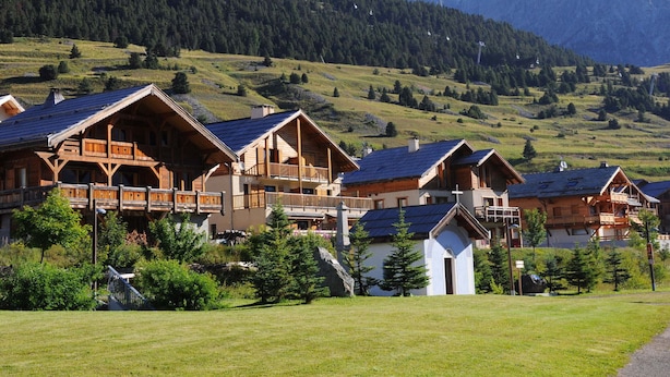 A row of wooden chalets with sloped roofs, set against a backdrop of green hills and mountains. - Functional apartment for 5 people with pets allowed, parking and south-facing balcony (Montgenèvre)