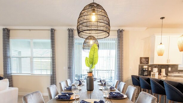 A modern dining area with a long wooden table, grey upholstered chairs, and a hanging light fixture. - Amazing 6BR Villa Private Pool & Theater (Kissimmee)