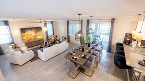 A modern living room with a large TV, a fireplace, and a dining area with a long table set for six. - Amazing 6BR Villa Private Pool & Theater (Kissimmee)