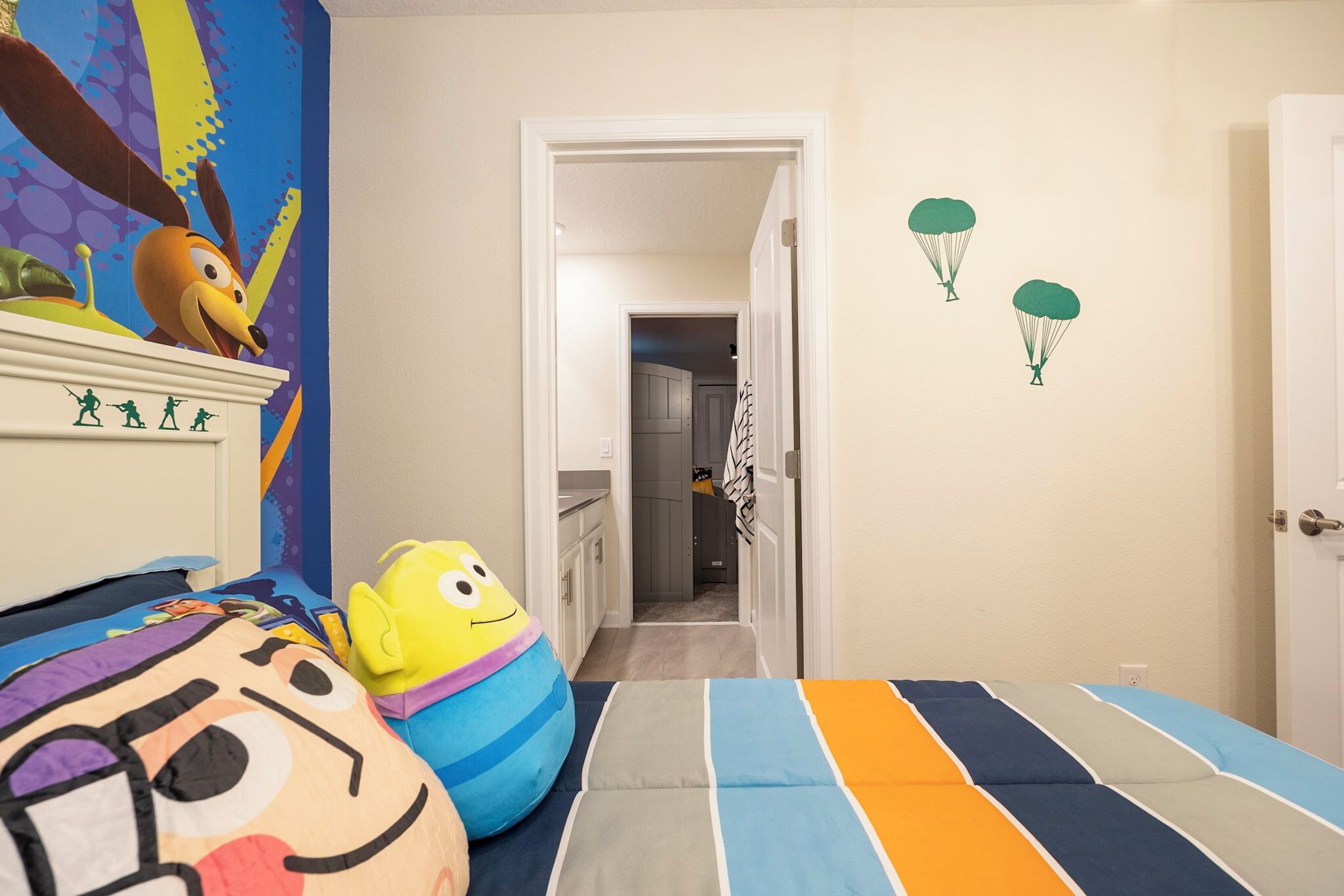 A child's bedroom with a bed, colorful pillows, a wall mural, and a door with a green balloon decal.