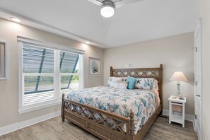 Une chambre à coucher avec un lit en bois, une table de chevet, une lampe et une fenêtre avec des stores.