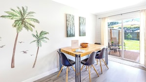 A dining area with a wooden table and black chairs, a white wall with palm tree decals, and a view of the backyard through a glass door. - BlueJay's Nest Unit B: Game Room, Walk to Water & Stadium (Clearwater)