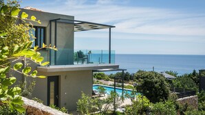 Ein modernes Haus mit einem Glasbalkon mit Blick auf einen Pool und das Meer.