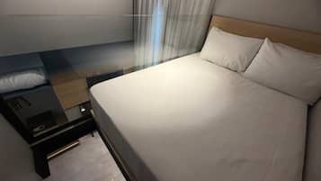 A hotel room with a bed, a nightstand, a drawer, a wooden headboard, and a window with curtains.