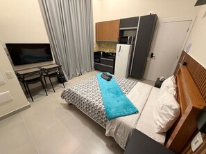 A bedroom with a bed, a TV, a desk, and a kitchenette. - Haus Mitre 370 (São Paulo)
