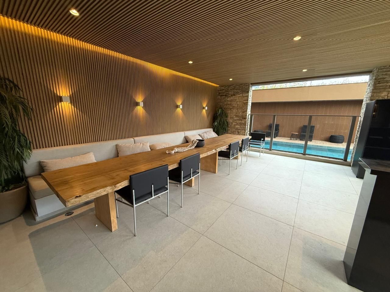 Uma área de estar moderna com uma mesa de madeira comprida, cadeiras pretas, um sofá e uma parede de pedra.