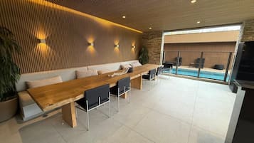 Uma área de estar moderna com uma mesa de madeira comprida, cadeiras pretas, um sofá e uma parede de pedra.