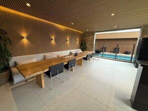 Ein moderner Loungebereich mit einem langen Holztisch, schwarzen Stühlen, einer Couch und einer Steinwand.