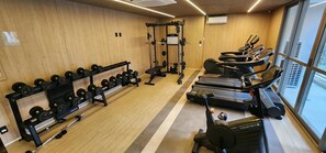 Un gimnasio con equipo de levantamiento de pesas, cintas de correr y una banca.