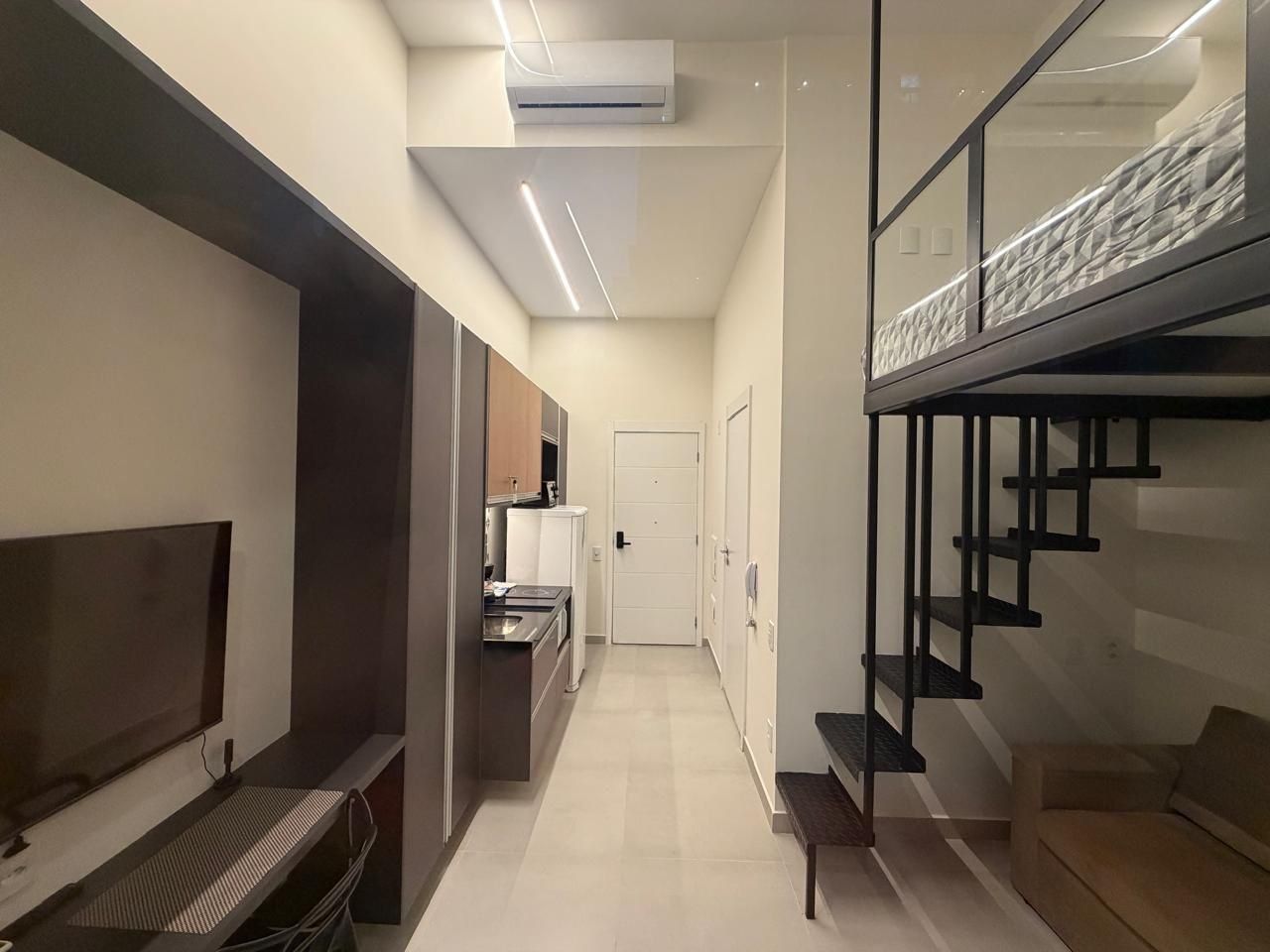A modern interior with a TV, kitchenette, staircase, and a door leading to another room.