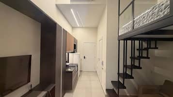 A modern interior with a TV, kitchenette, staircase, and a door leading to another room.